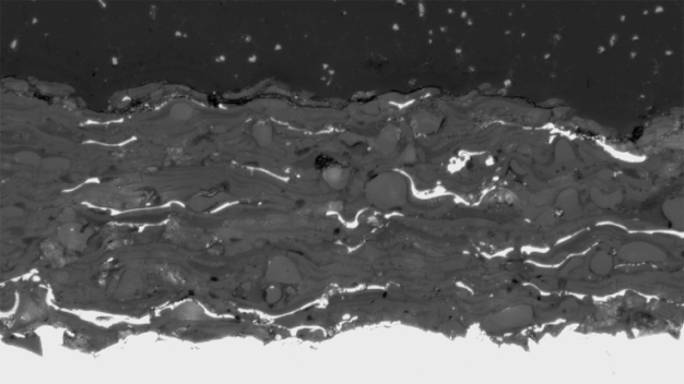 Querschliff einer kaltplasma-gespritzten Al2O3-Beschichtung (grau) mit 5% Cu (weiß). Oben: Einbettmasse, unten: Substrat. (INNOVENT e.V.)