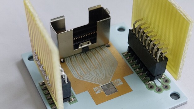 Darstellung der VCSEL-Quelle auf der Leiterplatte mit KOVAR-Rahmen. Im Rahmen ist die Optik untergebracht, die oben auf dem VCSEL-Chip befestigt ist. Die Glasspitze auf dem Gehäuse ist der Wellenleiterkombinator, aus dem das Polarisationssignal austritt. © Fraunhofer IOF / The VCSEL source on the ceramic printed circuit board (PCB) is shown with the KOVAR frame housing. The tiny glass tip on top of the housing is the waveguide combiner, where the polarization signal comes to exit. © Fraunhofer IOF