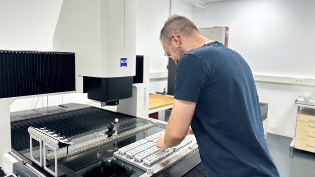 Lucas Schiem, Qualitätsprüfer richtet die Messvorrichtung für die Küvetten an der neuen Multisensor-Messmaschine ein. / Quality inspector Lucas Schiem sets up the measuring device for the cuvettes on the new multi-sensor measuring machine. 